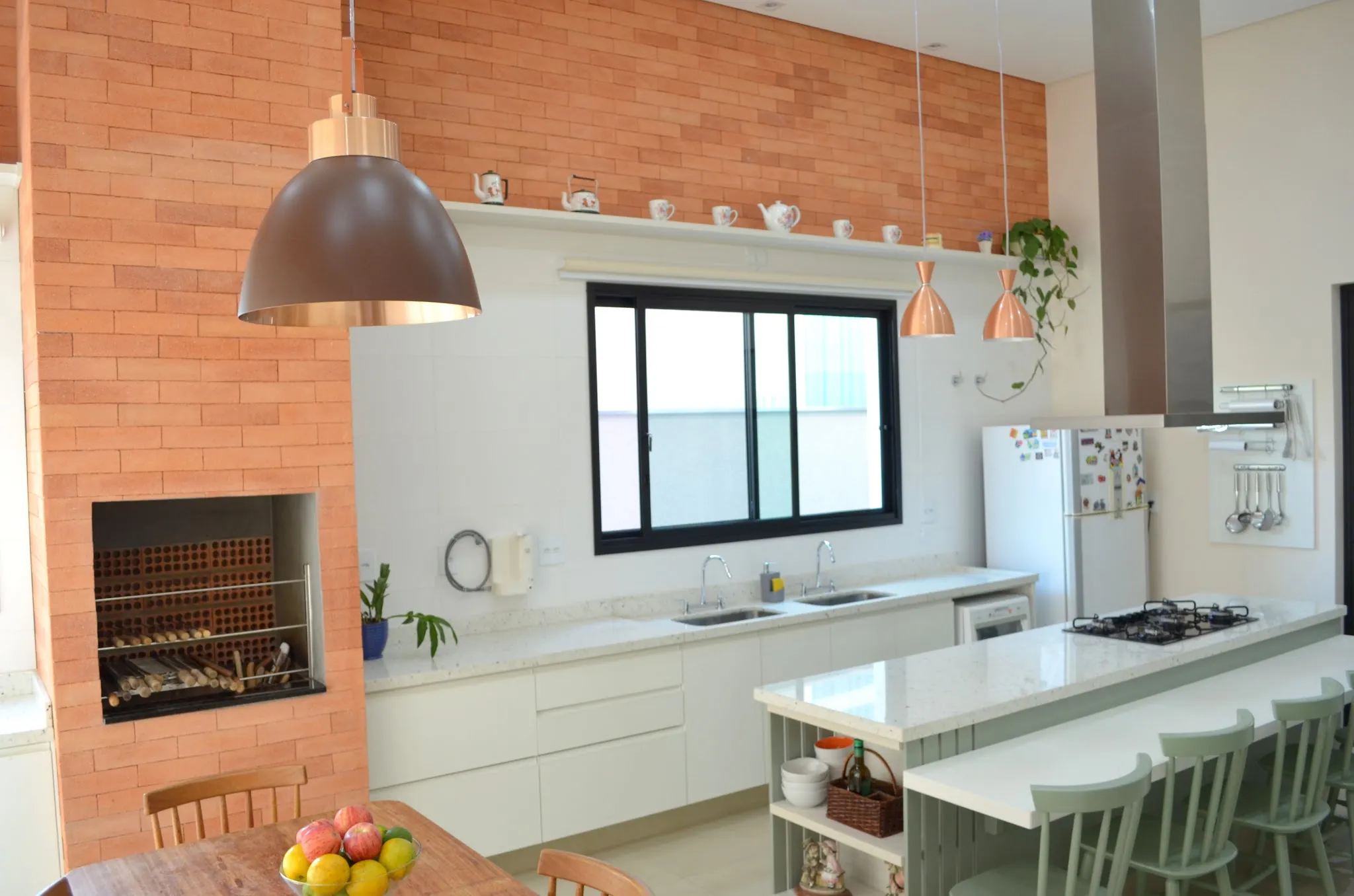 Área gourmet com ilha branca, banquetas verdes e churrasqueira de tijolo